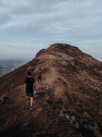 Rear view of man walking on mountain against sky