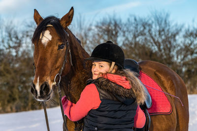 Portrait of young woman with brown horse on field during winter