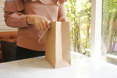 Midsection of woman holding paper bag on table at home