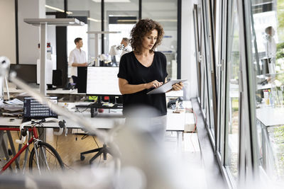 Businesswoman using digital tablet while working with colleague in background at open plan office