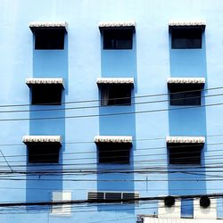 Low angle view of electricity cables against blue building