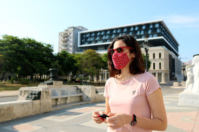 Portrait of young woman wearing facemask holding against built structure in old city