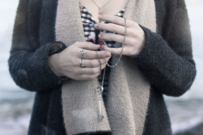 Midsection of young woman holding chain with key pendant at beach