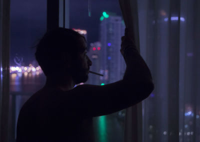 Side view of man looking through window night