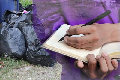 Digital composite image of person writing in book by garbage bags