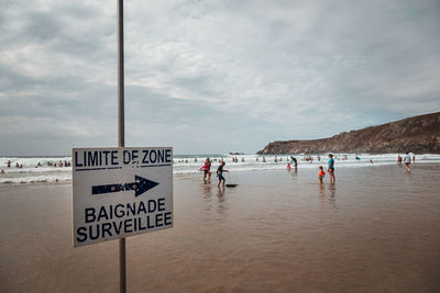 Information sign on beach against sky