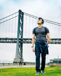 Full length of man listening music while walking on field against bridge and sky