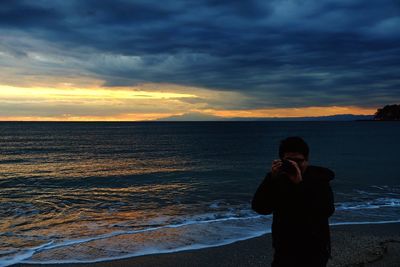 Woman standing on beach against sky during sunset