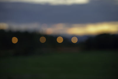 Defocused image of illuminated lights on field against sky at sunset