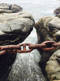 Close-up of rusty chain over rock formation sea