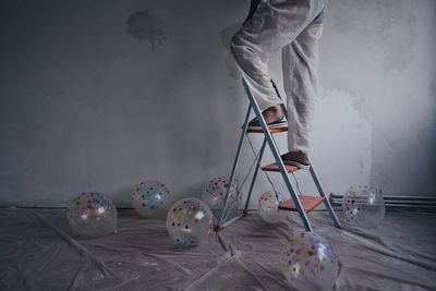 Low section of man standing on ladder against wall