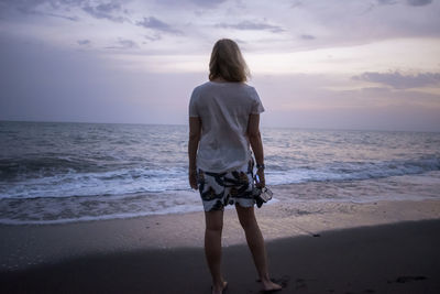 Rear view of woman standing at beach against sky