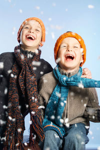 Happy siblings against sky during snowfall