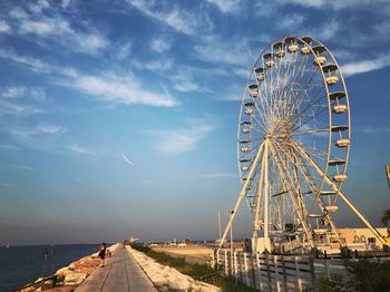 Ferris wheel at beach against cloudy sky