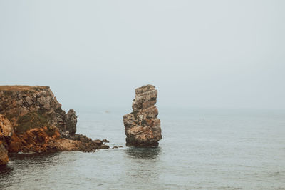 Rock formation in sea against clear sky