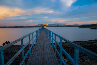 Bridge over calm reservoir against sky during sunset