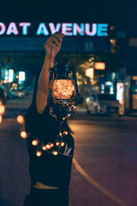 Woman photographing illuminated car on street at night