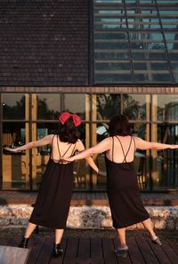 Portrait of 2 women in black backless dress against building