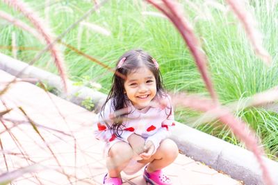 Portrait of smiling girl crouching on footpath against plants