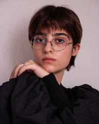 Portrait of young woman with eyeglasses against wall