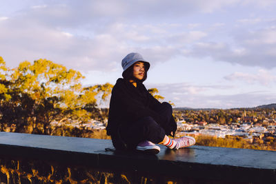 Young woman looking away while sitting against sky outdoors