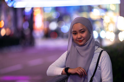 Portrait of smiling young woman standing in city at night