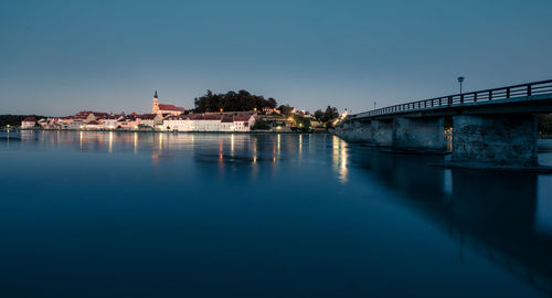 Bridge over river by buildings against clear blue sky