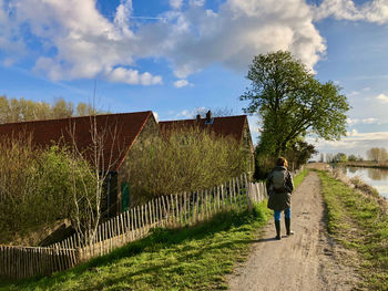 Rear view of woman walking at sunrise on a dike with at right a little river and farmhouses at left