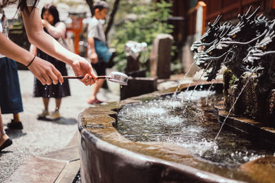 Cropped hands of woman holding ladle against fountain