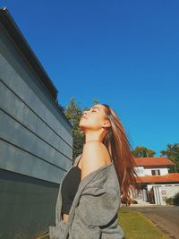 Low section of woman standing against building against clear blue sky