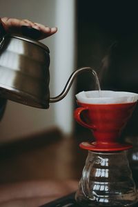 Close-up of hand pouring coffee in filter and cup