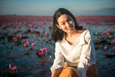 Portrait of young woman smiling while sitting against water lilies in pond