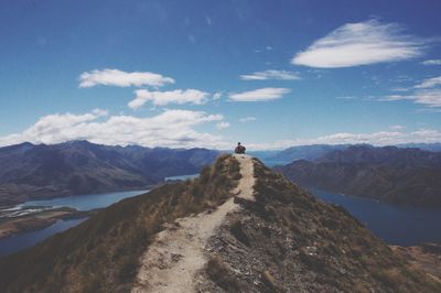 Rear view of person sitting on mountain surrounded by lakes