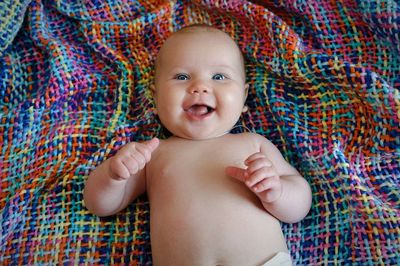 High angle portrait of shirtless cheerful baby girl lying on colorful sheet