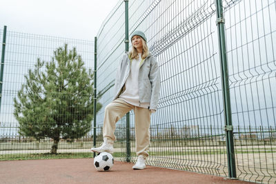 Teenage girl standing with soccer ball by fence at playground