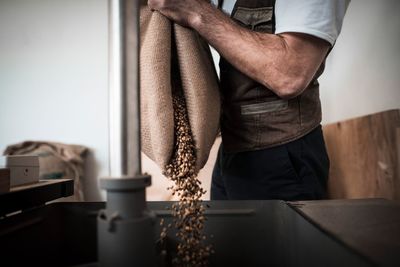 Midsection of man pouring coffee beans in coffee roaster