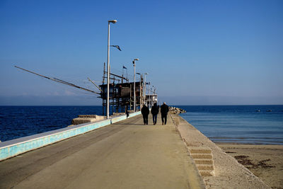 Rear view of people walking on jetty against sea