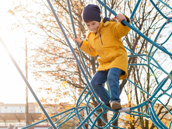 Little boy plays on children playground. kid climbs on rope structure on sports field. leisure