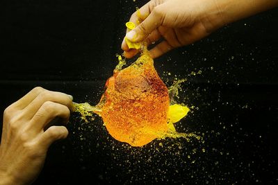 Cropped hands bursting water bomb against black background