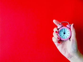 Close-up of hand holding clock against red background