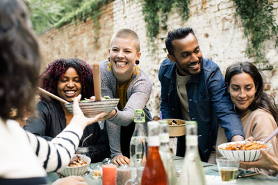 Young woman with toothy smile passing bowl to friend at dinner party