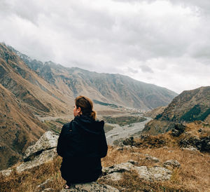 Rear view of woman sitting on mountain against sky