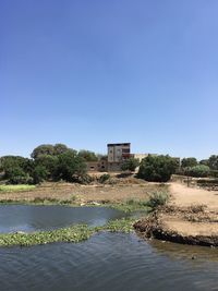 Scenic view of lake by building against clear blue sky