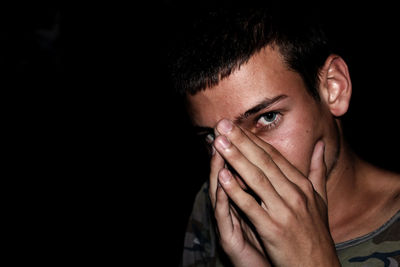 Close-up portrait of young man touching face against black background