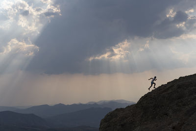 One man running up on a rock under a cloudy sky with sun rays