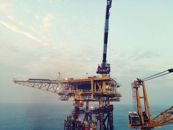 Cranes at commercial dock against sky