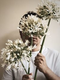 Midsection of man holding 3 stalks of white, agapanthus flowers.