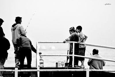 Rear view of people fishing in sea against clear sky