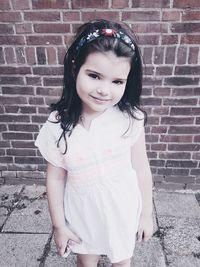 Portrait of smiling girl standing against brick wall