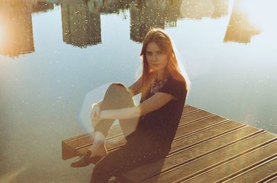 Portrait of young woman sitting by lake on jetty